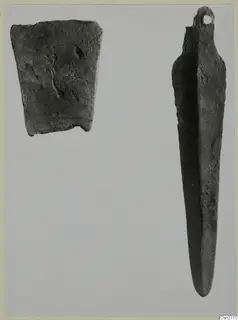 Two bronze objects from Lapithos: a flat corroded fragment and a long narrow tool with a loop at one end.