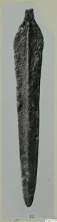 Corroded bronze blade with a short tang, photographed upright on a grey card mount.