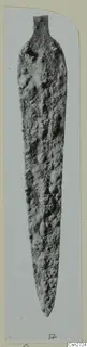 Corroded bronze blade with a narrow tang, photographed upright on a pale grey card