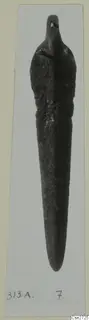 Bronze tool with a long tapering blade and a small knob at the top, photographed on a mount.