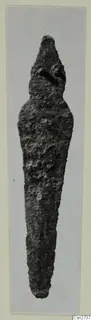 Long, tapering corroded metal object standing upright, photographed on a grey mount