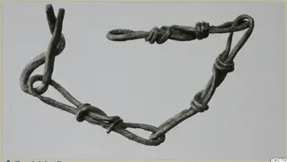 Bronze object of looped and coiled wire strands, photographed on a plain grey background