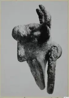 Corroded metal object with two upright prongs, a long downward-curving projection and a rod, on a pale background