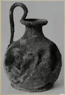 Bronze jug with a looped handle and a flared mouth, its surface encrusted with corrosion.