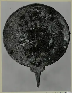 Corroded round bronze object with a narrow tang, from the Marion tomb finds (toilet-requisites)