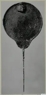 Bronze mirror with a round disc and long thin handle, photographed against a grey background