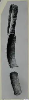 Corroded bronze strigil with a loop handle and a separate curved fragment below
