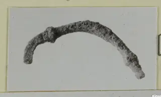 Corroded curved metal fragment, recorded as a bronze personal adornment, shown on a plain background.