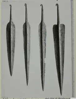 Four metal blades with pointed ends and curled hooked tangs, set upright side by side on a grey background.