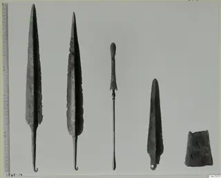 Five corroded metal points and implements set in a row beside a measuring scale