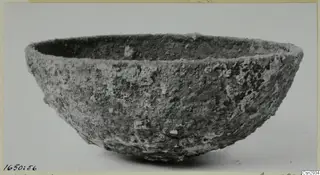 Heavily encrusted bowl with a wide mouth and rounded sides, seen from the side against a plain background.