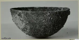 Bowl before conservation, with a rough, crusted dark surface and pale encrusted patches.