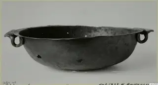 Dark metal bowl with a wide flaring rim and two loop handles, photographed on a pale background