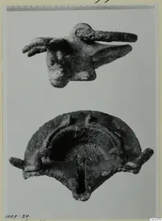 Two corroded metal objects: a small figure with a long projection above a curved, hollow object below