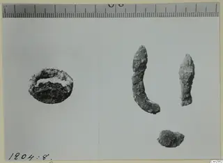 Four corroded metal fragments on a pale card, with a ruler along the top edge for scale