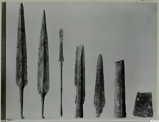 Seven corroded metal points, blades and fragments laid in a row beside a measuring rule