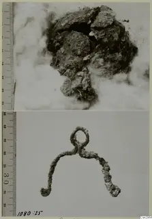 Two views of a corroded metal object: a crusted lump resting in cotton wool above, and a bent loop-shaped piece below.