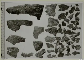 Sherds and fragments of pottery laid out on a pale grey board, with a measuring ruler along the left edge