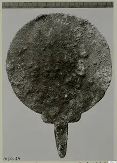 Corroded round metal disc with a narrow tang at its base.