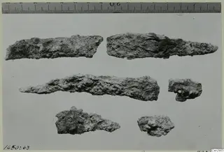 Six corroded metal fragments laid out before conservation, with a measuring ruler along the top edge