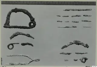Several corroded metal objects on a grey surface: a large open frame, curved rods, small rings and short fragments