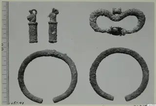 Several small metal objects before conservation: two loop-topped pendants, a figure-of-eight piece with a dark bead, and two open bangles.