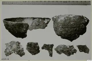 Two broken pottery vessels and five sherds laid out in a row, with a printed ruler along the top edge.