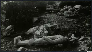 Carved stone fragment of a figure lying on grass among rocks and scrub on the Karpas peninsula