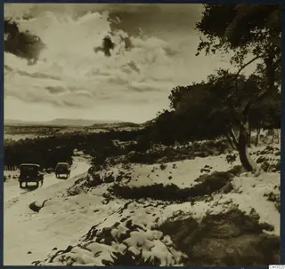 Snow-covered road with two vehicles driving past trees and hills near Kyrenia