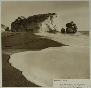 Aphrodite's Beach: a sandy shore with breaking surf, a large rock mass and offshore rock stacks in the sea