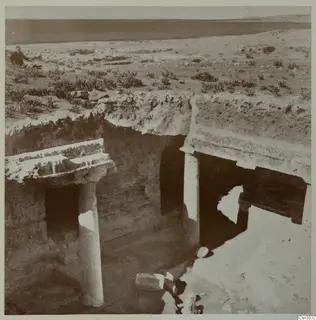 Excavated tomb openings at the Tombs of the Kings with two columns standing in a sunken court, a man at the upper left