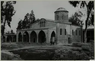 St Mamas Church, a stone church with a domed drum tower and an arched portico, with trees and a small group of people