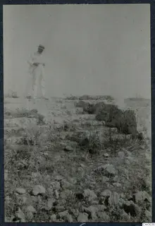 Man in a light suit and hat standing on a stepped stone ledge among scattered stones at Paphos