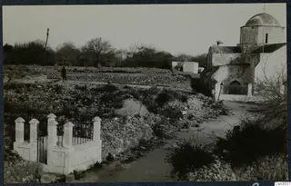Stone walls, a whitewashed domed church and a figure beside a dirt path at Paphos