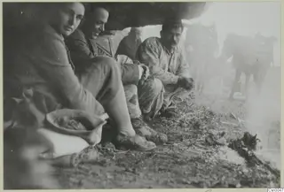 Four people sitting under a rock overhang, with two laden donkeys standing in the haze behind them
