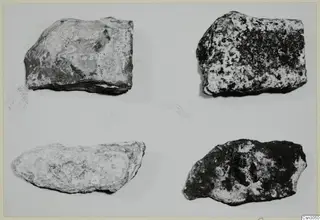 Fragments of stone tools: four rough stone pieces, two pale and two dark, on a pale background