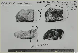 Four worked stone objects on a card with handwritten notes, dashed outlines of missing parts and a wooden handle sketch