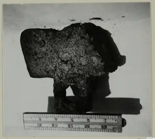 Corroded iron hoe with a round hole in its blade, shown beside a ruler.