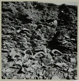Curved tubular pieces and flat broken fragments lying among soil, shown as parts and objects from copper mining