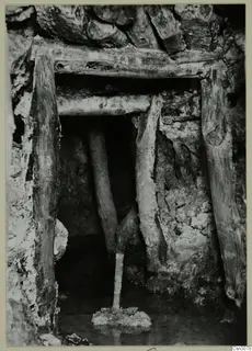 Entrance to a copper mine gallery framed by timber posts and a lintel, with water standing on the floor.