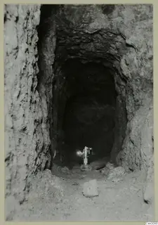 Narrow rock-cut gallery at Mavrovouni, with a lamp standing on the floor at its far end.