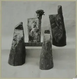 Four weathered wooden pieces standing on a light cloth, with a ruler laid between them.