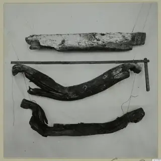 Three pieces of ancient timber, bent and distorted, laid out on a pale cloth with a measuring rod above them.