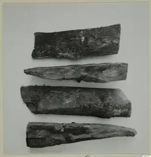 Four ancient wooden wedges lying in a row on a pale background.