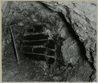 Crib-timbered shaft in rock face, with a rod placed alongside it
