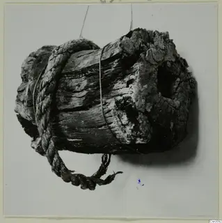 Rope wrapped around a weathered wooden object, a mining find photographed against a pale background