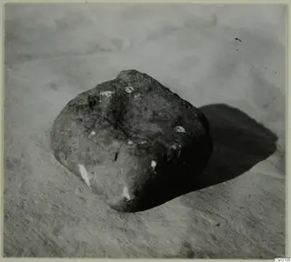 Rounded stone with white flecks, photographed on a plain surface; probably used as a base for a timber post.
