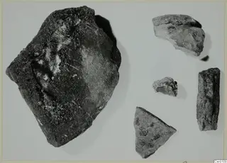 Five fragments of stone or pottery with dark slag accretions, photographed on a pale background.