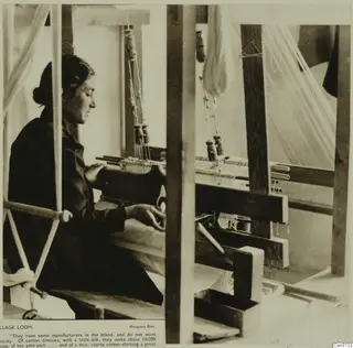 Woman seated at a wooden village loom, working the threads, seen from the side