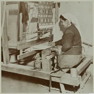 Woman weaving at a wooden loom, with a patterned textile hanging above the frame.